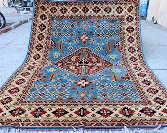 May include: A blue and red patterned rug with a central diamond shape. The rug has a fringe border and intricate details.