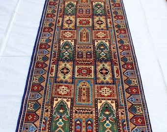 Könnte beinhalten: Ein langer, rechteckiger Teppich mit einem farbenfrohen geometrischen Muster. Der Teppich hat einen blauen Rand mit komplizierten Designs und ein zentrales Feld, das mit Quadraten und Rechtecken in Rot-, Grün-, Blau- und Gelbtönen gefüllt ist.