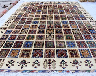 May include: A cream-coloured rug with a geometric pattern of colourful squares. The rug has a fringe border and is made of wool.