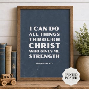 May include: A framed wall art print featuring a dark blue background with white text that reads I CAN DO ALL THINGS THROUGH CHRIST WHO GIVES ME STRENGTH and PHILIPPIANS 4:13. The poster is displayed in a brown wooden frame on a shelf.