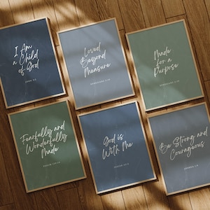 Puede incluir: Seis impresiones artísticas enmarcadas con citas inspiradoras en escritura blanca sobre varios fondos de colores. Las impresiones incluyen frases como "Soy un hijo de Dios" y "Sé fuerte y valiente". Cada impresión tiene un marco de madera.