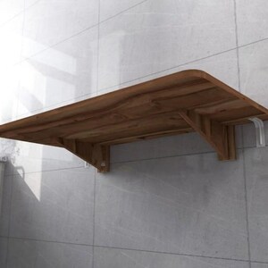 May include: A brown wooden folding wall-mounted table with white metal brackets. The table is mounted to a tiled wall.