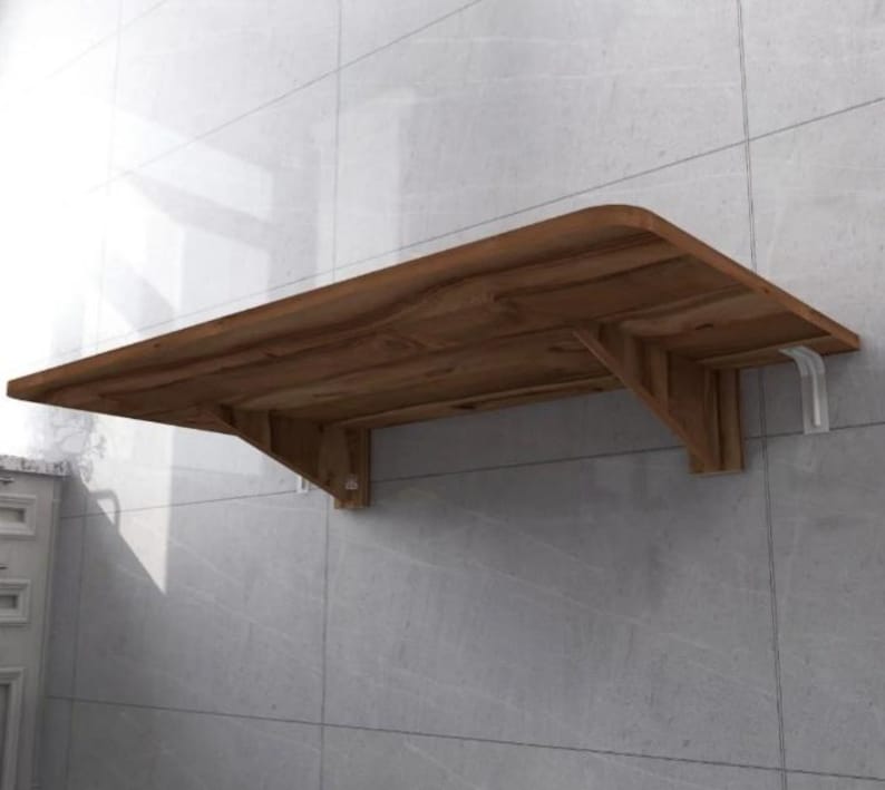 May include: A brown wooden folding wall-mounted table with white metal brackets. The table is mounted to a tiled wall.