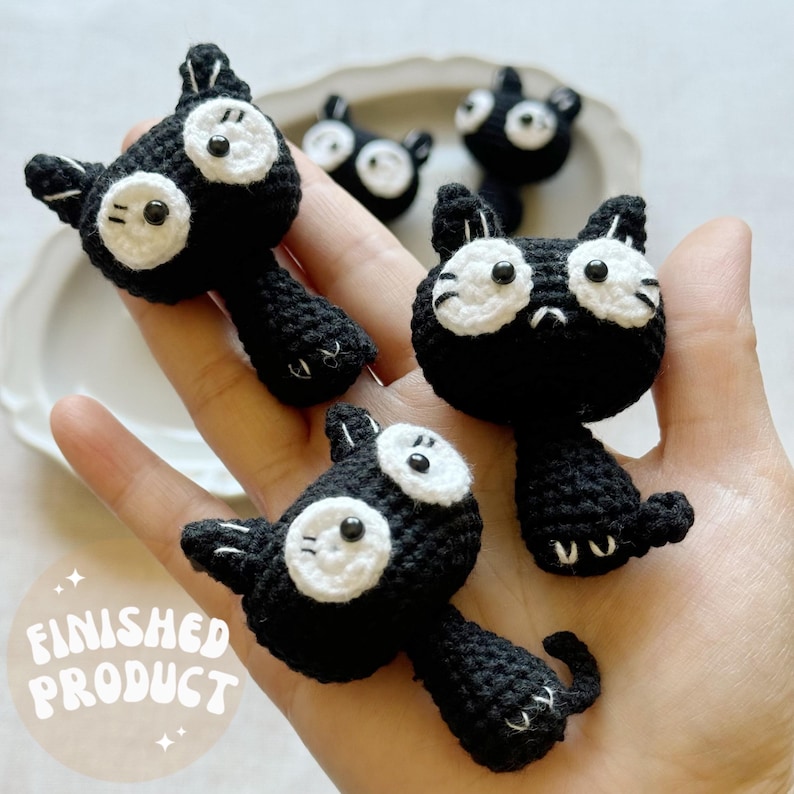 May include: Handmade black crochet cat figures with white eyes and accents. The figures have a whimsical design and are displayed on a light background. The text "FINISHED PRODUCT" is visible in the image.