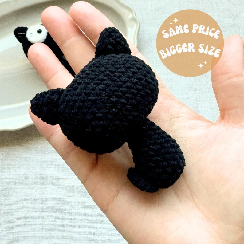May include: A handmade black crochet bat with outstretched wings. The bat is held in a hand, with a smaller black and white crochet bat in the background. The image includes a circular sticker with the text "SAME PRICE BIGGER SIZE".