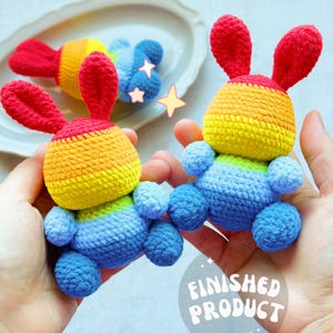 May include: Crocheted rainbow bunny toys with red ears, yellow, orange, and blue bodies, and blue feet. The text "FINISHED PRODUCT" is visible in a white circle. The toys are handmade and colorful.