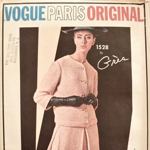 May include: A vintage Vogue Paris Original sewing pattern featuring a pink tweed suit designed by Grès. The pattern number is 1528.