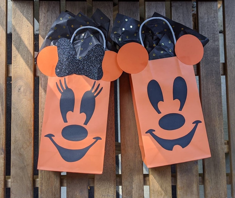 May include: Two orange Halloween treat bags with black Mickey Mouse faces. The bags have black tissue paper peeking out of the top.
