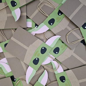 Może przedstawiać: Kolekcja brązowych papierowych torebek na prezenty, każda ozdobiona zielonym, r&oacute;żowym i czarnym wzorem postaci. Torby mają beżowe uchwyty i są ułożone w zbliżeniu, zachodzącym na siebie wzorze.