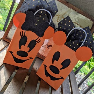 May include: Two orange Halloween treat bags with black Mickey Mouse faces. The bags have black and gold polka dot tissue paper inside.
