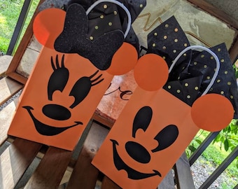May include: Two orange Halloween treat bags with black Mickey Mouse faces. The bags have black and gold polka dot tissue paper inside.