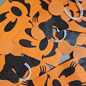 May include: Orange paper bags with black and white smiling faces. The bags have white handles and black glitter accents.