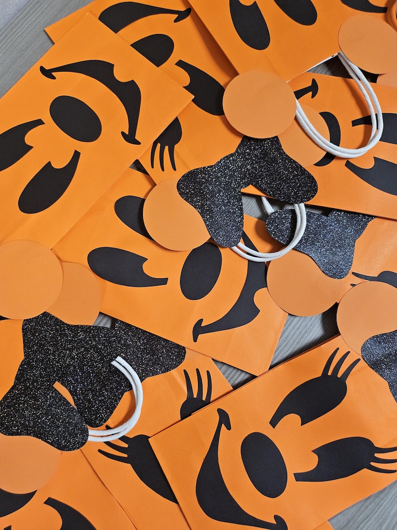 May include: Orange paper bags with black and white smiling faces. The bags have white handles and black glitter accents.