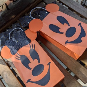 May include: Two orange Halloween treat bags with black Mickey Mouse and Minnie Mouse faces. The bags have black glitter accents and white string handles.