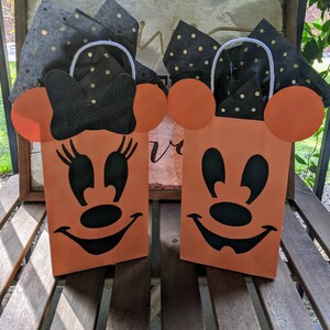 May include: Two orange Halloween treat bags with black Mickey Mouse and Minnie Mouse faces. The bags have white handles and are filled with black and gold tissue paper.