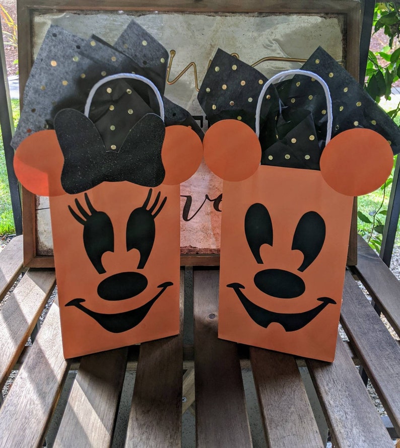 May include: Two orange Halloween treat bags with black Mickey Mouse and Minnie Mouse faces. The bags have white handles and are filled with black and gold tissue paper.