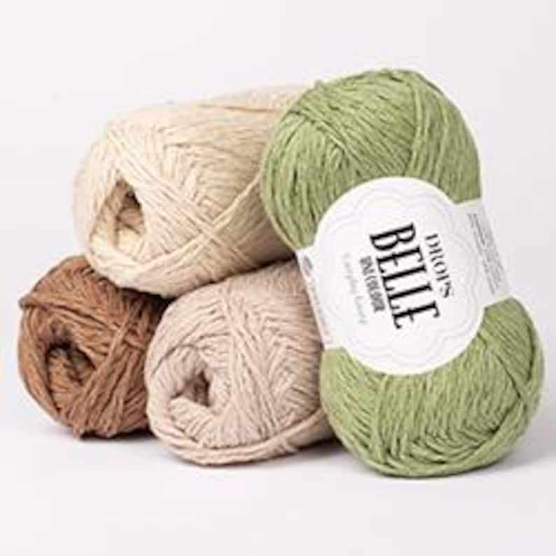 May include: A collection of yarn skeins in various colors, including beige, brown, and green. One skein has a label that reads "DROPS BELLE". The yarn appears to be soft and suitable for knitting or crocheting projects. The skeins are stacked together.