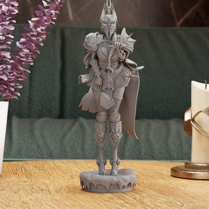 May include: A grey 3D printed figurine of a female warrior wearing armour and a crown. The figurine is standing on a base with a textured surface.
