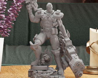 May include: A gray figurine of a muscular character holding two large futuristic guns. The figure is wearing armor and a utility belt. The statue is on a rocky base, with a detailed design. The background includes a green cloth and a wooden surface.