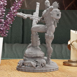 May include: A gray figurine of the comic book character Spawn, standing on a base with a skeleton and skulls. Spawn is holding a severed head and a cross. The figurine has detailed armor and spiked accents.