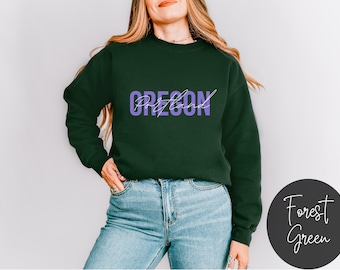 May include: A dark green sweatshirt with the text "OREGON" in purple lettering. The sweatshirt is being worn by a person with long brown hair.
