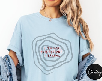 May include: Light blue t-shirt with the text "I THINK, THEREFORE I SPIRAL" in red and a gray spiral design. The shirt is a casual style, with rolled-up sleeves.