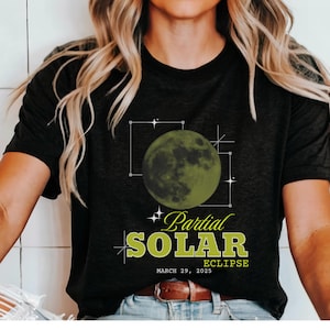 May include: Black t-shirt featuring a green graphic of a partial solar eclipse. The design includes a green moon, geometric lines, and the words "Partial Solar Eclipse, March 29, 2025" in a retro font. A casual tee for astronomy enthusiasts.