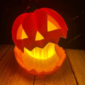 May include: A lit orange Halloween pumpkin with triangular eye and mouth cutouts. The pumpkin sits on a wooden surface, with a warm glow emanating from within. The background is dark.