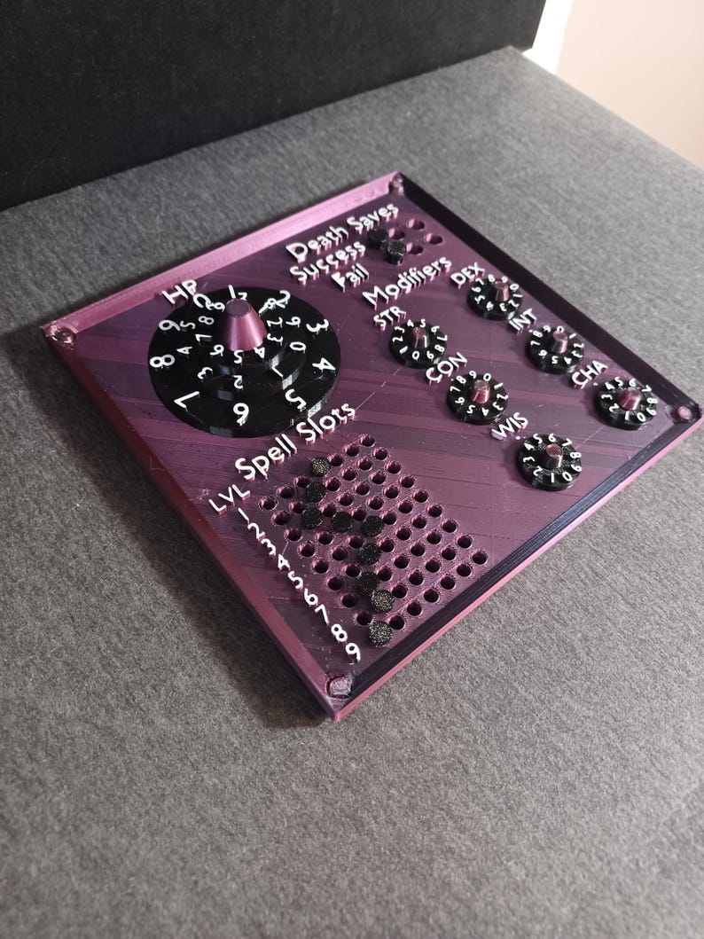 May include: A purple and black 3D printed tabletop game tracker with dials for hit points, death saves, modifiers, and ability scores. The tracker also includes a grid for spell slots.