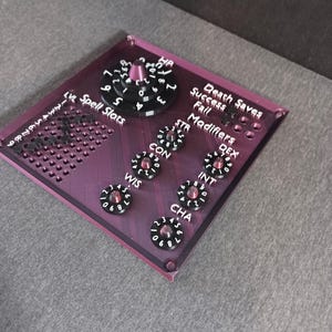 May include: A purple acrylic tabletop game board with a black dial for hit points, a grid for spell slots, and dials for ability scores, including strength, dexterity, constitution, wisdom, intelligence, and charisma. The board also includes a section for death saves with success and fail indicators.