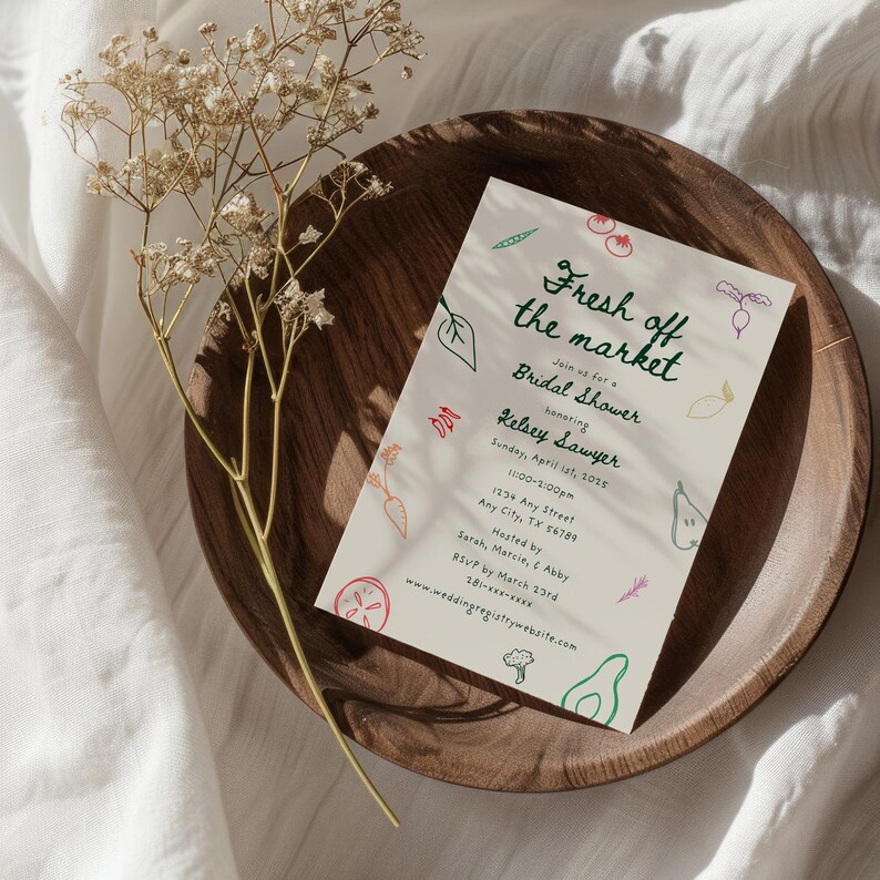 May include: A white invitation card with green text that reads "Fresh off the market" and "Bridal Shower honoring Kelsey Sawyer". The card is decorated with colorful illustrations of vegetables and fruits.