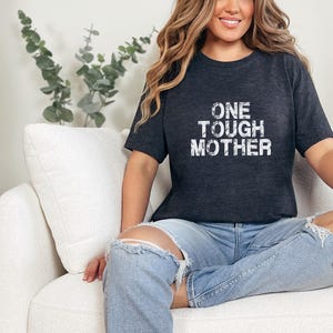 May include: A heather dark grey t-shirt with the text "ONE TOUGH MOTHER" printed in white on the front.