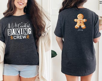 May include: Dark gray t-shirt with the text "Cookie Baking Crew" in white and orange. The back of the shirt features a gingerbread man graphic and the name "James". The shirt is a heather dark gray color.