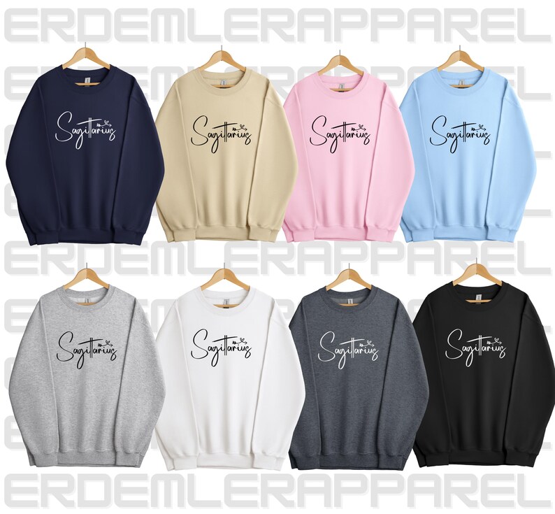 K&ouml;nnte beinhalten: Ein Set aus zehn Crewneck-Sweatshirts in verschiedenen Farben, jedes mit dem Text "Sagittarius" in einer handschriftlichen Schriftart. Die Sweatshirts sind in Marineblau, Beige, Rosa, Hellblau, Grau, Wei&szlig;, Dunkelgrau und Schwarz erh&auml;ltlich.