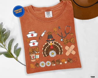 May include: Burnt orange Comfort Colors t-shirt featuring a cartoon turkey wearing a pilgrim hat and medical-themed graphics. Includes nurse hats, a syringe, a stethoscope, and a bow tie with a leopard print.