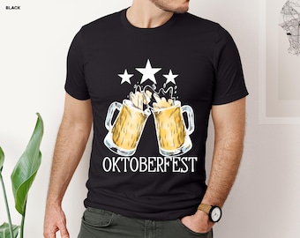 May include: Black t-shirt featuring a graphic of two beer steins clinking, with beer overflowing. Above the steins are three white stars. The word "OKTOBERFEST" is printed in white below the steins.