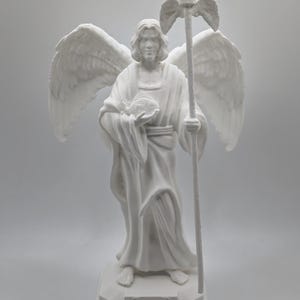 Peut inclure: Statue blanche de l'archange Raphaël avec des ailes, tenant un bâton et un globe. La statue est posée sur un socle avec l'inscription "St. Raphaël".