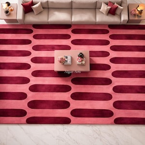 Pode incluir: Vista aérea de um tapete retangular grande com um padrão repetitivo de ovais bordô sobre um fundo rosa. O tapete está em uma sala de estar, com um sofá, mesas laterais e uma mesa de centro.