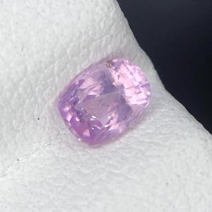 Puede incluir: Una piedra preciosa de color rosa claro translúcido, con talla cojín y una superficie facetada que refleja la luz. La piedra muestra un tono rosa suave y uniforme en toda su estructura, con un aspecto claro y pulido de bordes definidos.