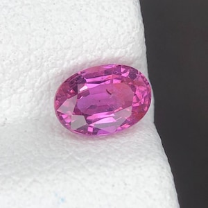 Puede incluir: Una gema rosa de corte ovalado con una superficie facetada que refleja la luz. La piedra muestra un tono magenta intenso con claridad interna y bordes definidos, exhibiendo un corte clásico diseñado para engastes de joyería.