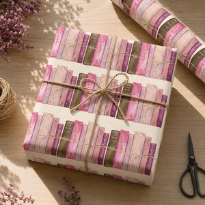 Könnte beinhalten: Ein rechteckiges Geschenkpaket, eingewickelt in cremefarbenes Papier mit einem wiederkehrenden Muster aus vertikalen Büchern in Rosa-, Mauve- und Brauntönen. Das Paket ist mit einer dünnen braunen Schnur zu einer Schleife gebunden, daneben liegt eine Rolle.