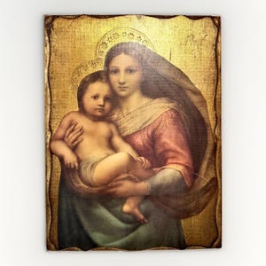 May include: A rectangular wall plaque featuring a classical painting of a woman holding a child. The woman wears a dark head covering and a reddish-pink garment, while the child is unclothed. The background is a textured, metallic gold leaf.