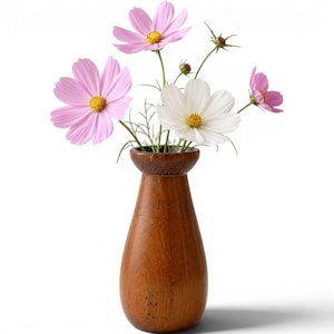 May include: A smooth, medium-brown wooden vase with a flared rim holds a bouquet of delicate cosmos flowers. The arrangement features two large pink blossoms, one white blossom, and one smaller pink bud, all with bright yellow centers and thin stems.