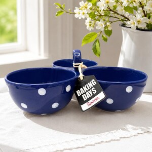May include: A dark blue ceramic triple-bowl server with white polka dots and a central handle. A black rectangular tag is attached to the handle with a string, featuring the white text BAKING DAYS and the red Spode logo at the bottom.