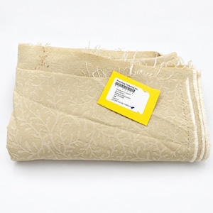 May include: A folded piece of light beige fabric featuring a tonal, raised leaf and vine pattern. A bright yellow rectangular tag is attached to the fabric, printed with the text Premiere Finishing Inc., SKYVIEW, BEESWAX, and CEDAR RIDGE FABRICS.