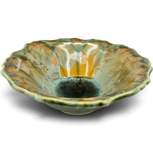May include: A shallow ceramic bowl with a scalloped edge, featuring a crystalline glaze that transitions from a deep dark blue center to shades of amber, gold, and sage green, with radiating feather-like patterns across the interior surface.