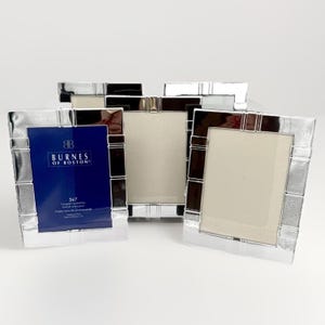 May include: Several silver-colored picture frames with a rectangular design. One frame displays a blue card with the text "BURNES OF BOSTON" and "5x7". The frames have a reflective, metallic finish.