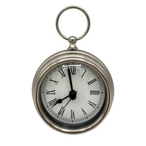May include: A round silver-toned metal wall clock featuring a white face with black Roman numerals and black hour, minute, and second hands. The clock has a circular metal ring at the top for hanging and a clear glass cover over the dial.