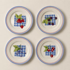 May include: A set of four round ceramic plates with a cream-colored base, each featuring a blue and white checkered square pattern in the center. The plates are decorated with illustrations of strawberries, blackberries, blueberries, and cherries.