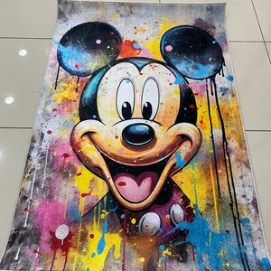 May include: A rectangular area rug featuring a large, centered illustration of Mickey Mouse. The design incorporates a vibrant, multi-colored paint splatter effect with drips of black, yellow, blue, and pink against a textured gray background.